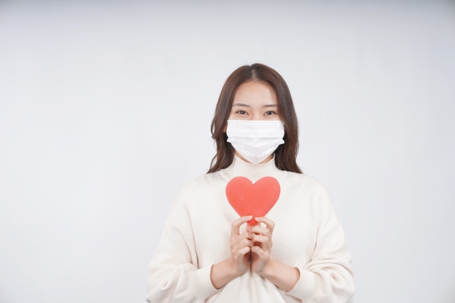 マスクをしてハートを持っている年下女性